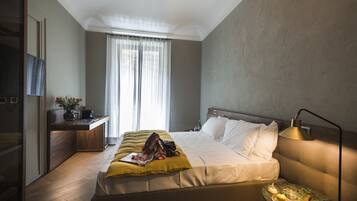 A hotel room with a bed, bedside table, lamp, and a view of the outdoors through the window.
