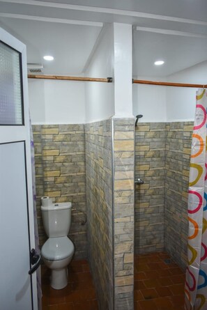 Un baño con inodoro, cabina de ducha y pared con azulejos.