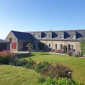 A stone building with a sloped roof, a red door, and a patio with outdoor seating.