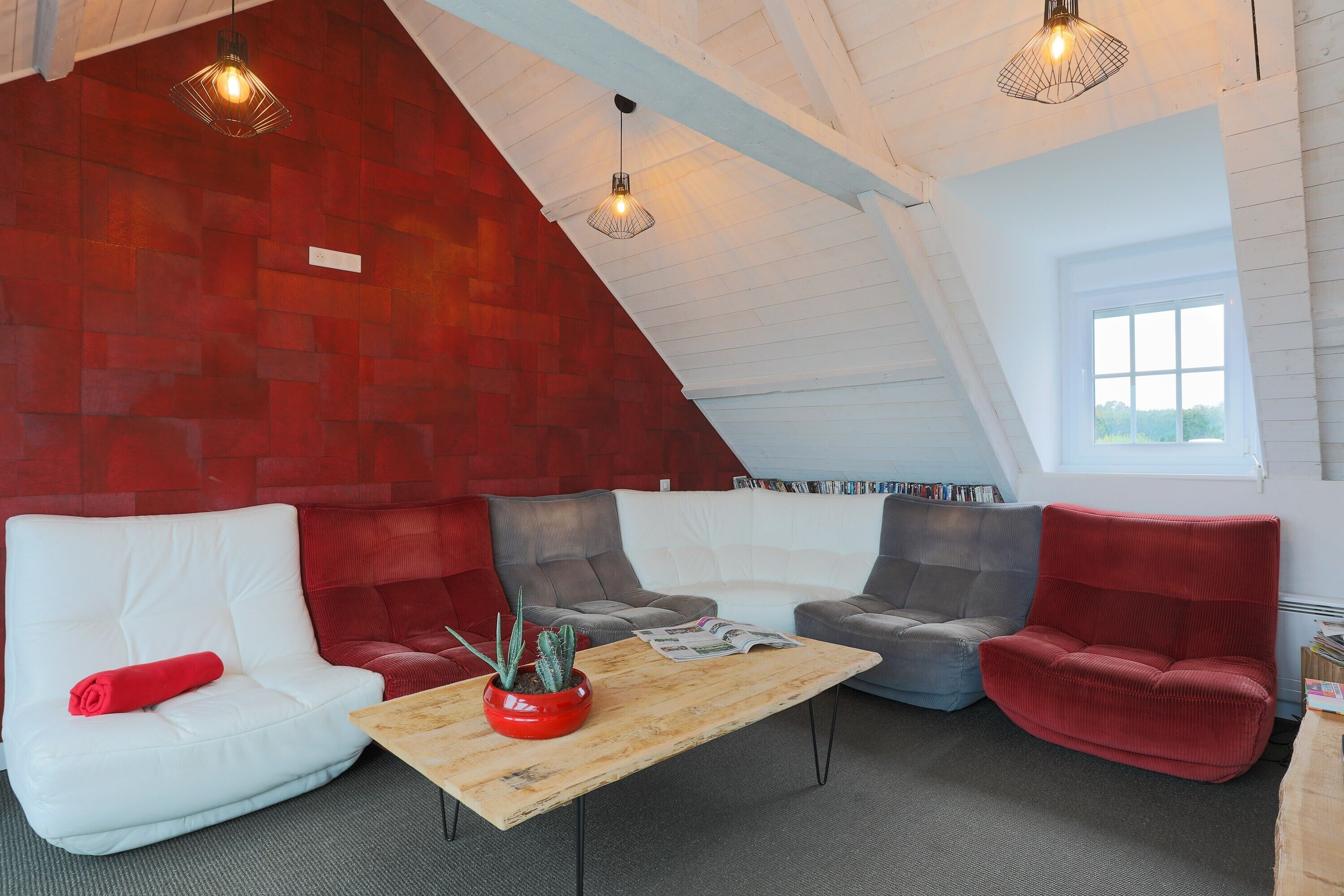 A cozy loft with a sloped ceiling, red brick walls, and a mix of white and grey upholstered seating.
