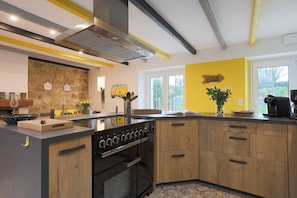 A modern kitchen with a stone backsplash, wooden cabinets, a built-in stove, and a large window.