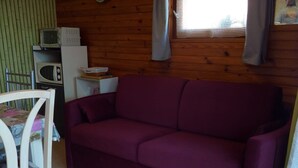 A wooden interior with a purple sofa, a white chair, a microwave, and a small table with a box on it.