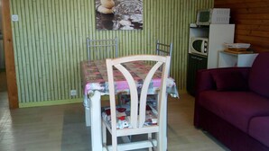 A dining area with a table and chairs, a wooden wall with vertical blinds, a television, and a purple sofa.