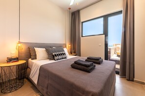 Ett modernt hotellrum med en stor säng, två sänglampor, ett litet runt bord och utsikt över omgivningarna genom ett stort fönster.