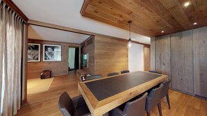 Een moderne eethoek met een houten tafel en stoelen, een televisie en kunstwerken in lijsten aan de wanden.