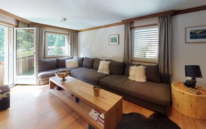 A modern living room with a sectional sofa, a wooden coffee table, and a side table with a lamp. - Modern in alpine style designed apartment with tasteful details (St. Moritz)