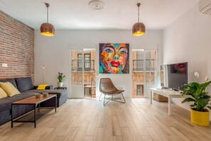 A modern living room with a sofa, a coffee table, a chair, a TV, and a large painting on the wall.