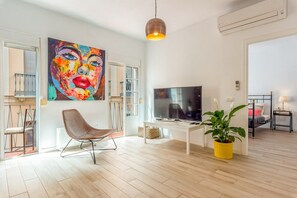 A modern living room with a flat-screen TV, a woven chair, a potted plant, and a colorful abstract painting. - Julia Centro Historico | Charming Top Floor Apartment with Balcony in the Heart of Malaga (Málaga)