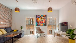 A modern living room with a sofa, a coffee table, a chair, a TV, and a large painting. - Julia Centro Historico (Málaga)
