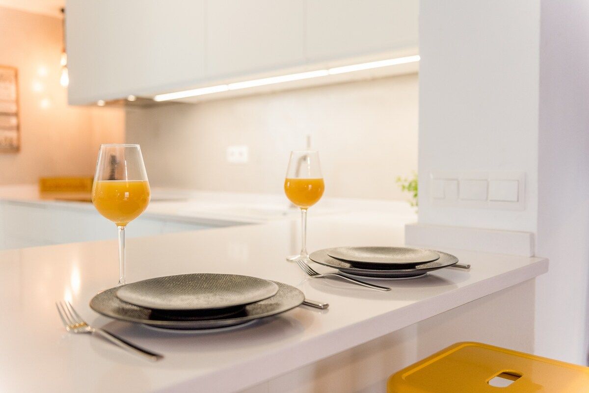 A modern kitchen with two dining sets, each with a glass of orange juice, on a white countertop.