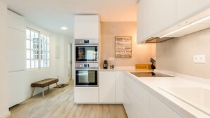 A modern kitchen with white cabinetry, a built-in oven, a coffee machine, and a wooden bench. - Julia Centro Historico (Málaga)