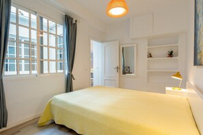 A bedroom with a bed, a window with curtains, a bedside lamp, and a mirror on the wall. - Julia Centro Historico | Charming Top Floor Apartment with Balcony in the Heart of Malaga (Málaga)