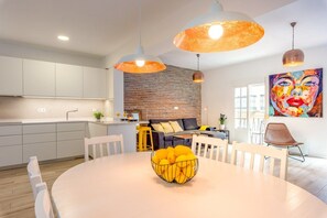 Une cuisine moderne avec des meubles blancs, un coin repas doté d’une table ronde et un espace de vie comprenant un canapé et un tableau coloré.