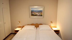 Ein Doppelbett mit weißen Bettwäsche, zwei Nachttischlampen und ein gerahmtes Landschaftsbild an der Wand.