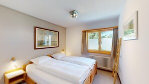 Un dormitorio con dos camas, una ventana, un radiador y un cuadro enmarcado en la pared.