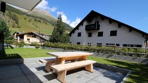 Ein Holztisch mit Bänken in einem Innenhof, im Hintergrund Berge.