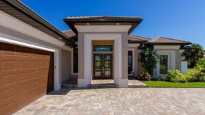 A residential property with a brick driveway, a garage, a covered entrance, and a well-maintained lawn. - Coral Paradise- Salt Water Pool - baby fence (Cape Coral)