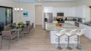 A modern kitchen with white cabinets, stainless steel appliances, and a marble island with bar stools. - Coral Paradise- Salt Water Pool - baby fence (Cape Coral)