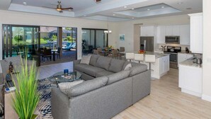 A spacious living area with a grey sectional sofa, a glass coffee table, and a ceiling fan. - Coral Paradise- Salt Water Pool - baby fence (Cape Coral)