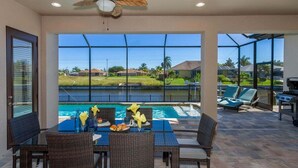A covered outdoor area with a pool, dining table, chairs, and lounge chairs. - Coral Paradise- Salt Water Pool - baby fence (Cape Coral)