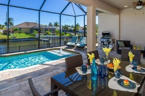 Un espace repas aménagé au bord de la piscine, offrant une vue sur la piscine et sur une maison en arrière-plan.