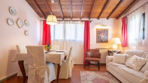 Zona pranzo con tavolo apparecchiato per due, un divano e un quadro appeso al muro.