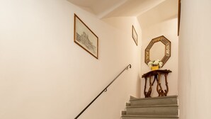 Una scala con corrimano, un tavolino consolle in legno con un vaso di fiori e quadri appesi alle pareti.