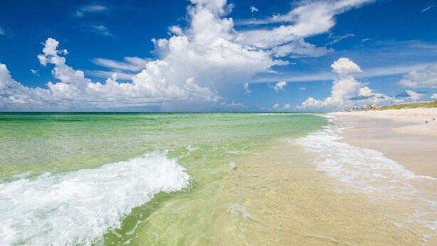 Una playa con aguas turquesas cristalinas, arena blanca y cielo despejado.