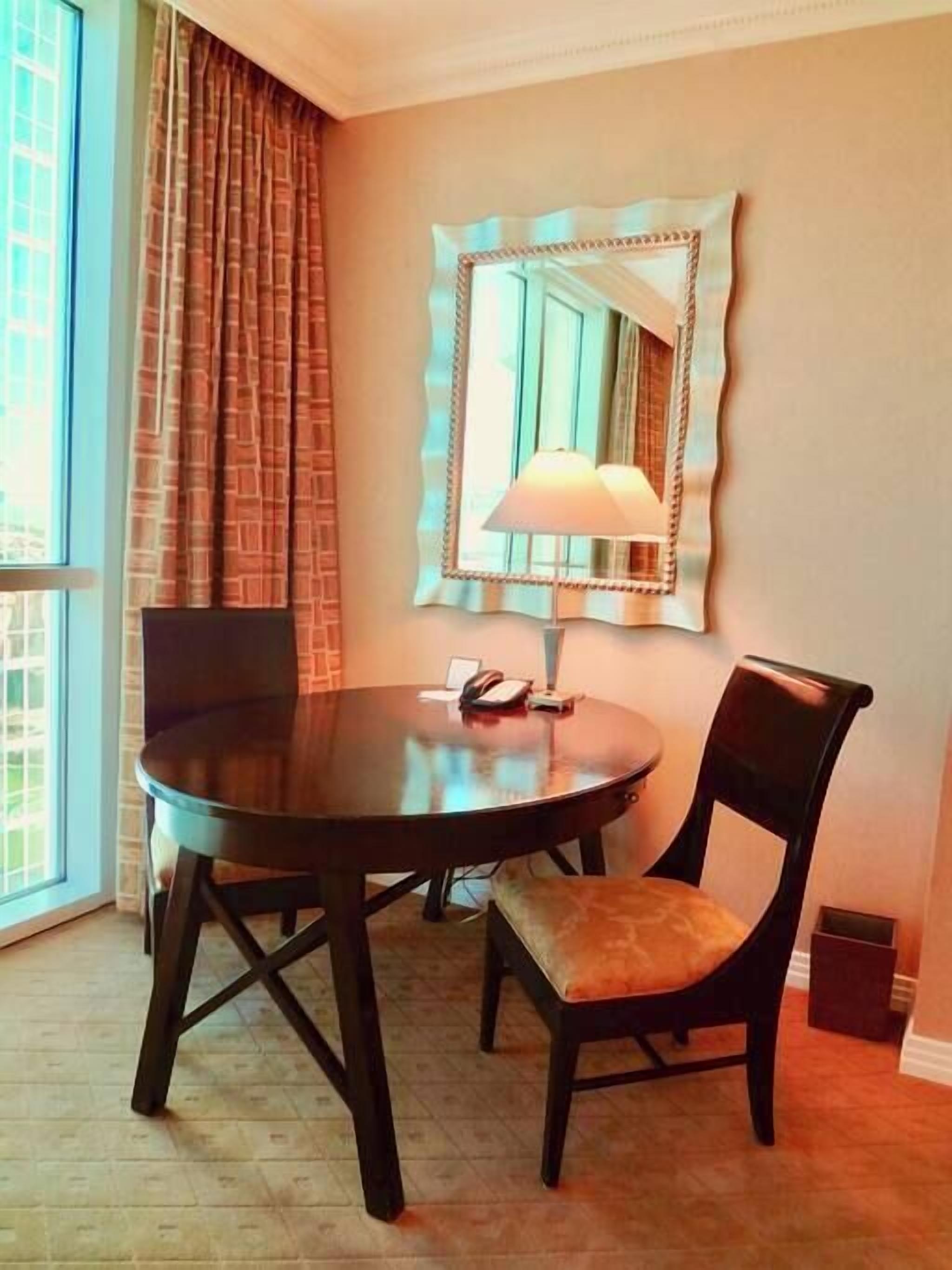 A room with a round table, two chairs, a lamp, and a mirror on the wall.