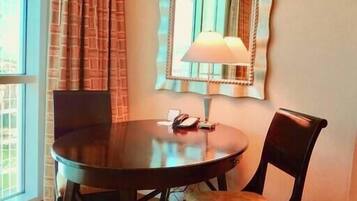 A room with a round table, two chairs, a lamp, and a mirror on the wall.