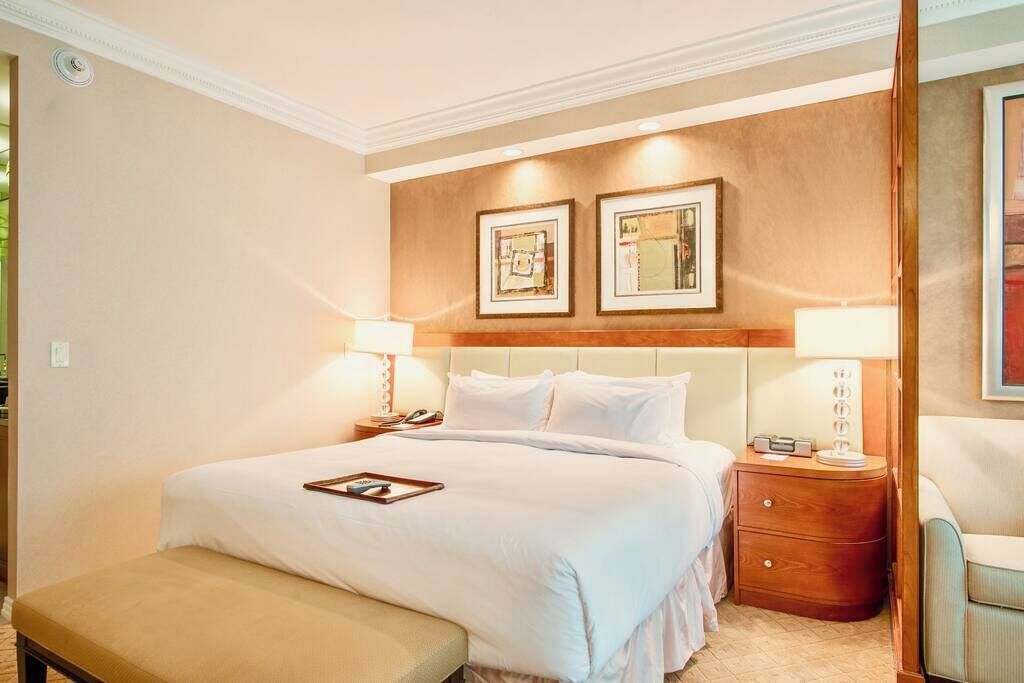 A hotel room with a large bed, two bedside tables, a bench, and framed pictures on the wall.