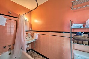 A bathroom with pink tiles, a bathtub, a toilet, and a shelf with towels and toiletries. - Walk to Shops, Dining & City Park: Reading Apt (Reading)