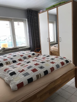 A bedroom with a bed, a wardrobe, and a window with curtains. - Small, cozy holiday home in a quiet location in the old town for 2-4 people (Friedrichstadt)