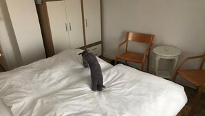 Una cama con ropa de cama blanca, una almohada a rayas y una silla de madera al lado.