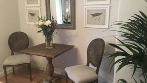 Un coin repas avec une table en bois, deux chaises, un vase de fleurs et des tableaux représentant des oiseaux accrochés au mur.