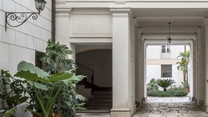 Um pátio com piso de pedra, plantas em vasos e uma escadaria que leva a um andar superior.