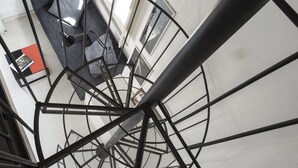 Escadaria em espiral com corrimão de metal, um sofá cinza com almofadas e uma janela com vista para uma montanha.