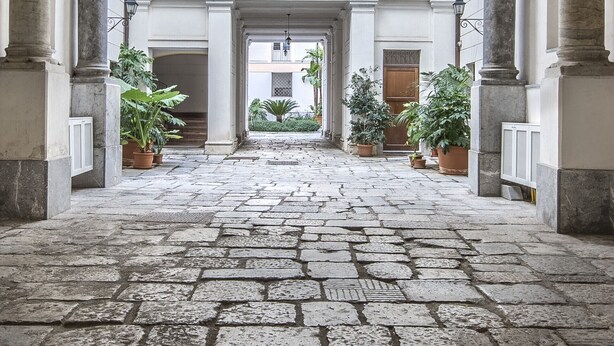 Um pátio com piso de pedra, arcos, colunas e vasos de plantas.