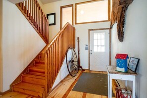 A wooden staircase with a handrail, a door with a window, a wall-mounted clock, and a small table with a decorative house and a framed picture. - Dancing Bear - Private Wooded Lot, Dog Friendly (Davis)