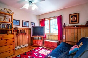A cozy living room with a television, wooden furniture, a bookshelf, and a window with curtains.