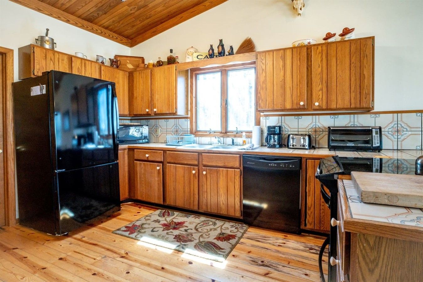 A kitchen with wooden cabinets, a black refrigerator, a dishwasher, a microwave, and a toaster.