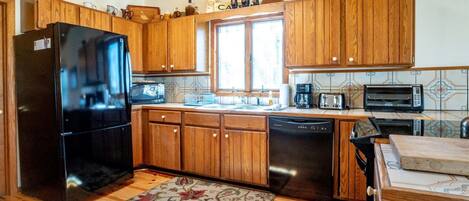 A kitchen with wooden cabinets, a black refrigerator, a dishwasher, a microwave, and a toaster.