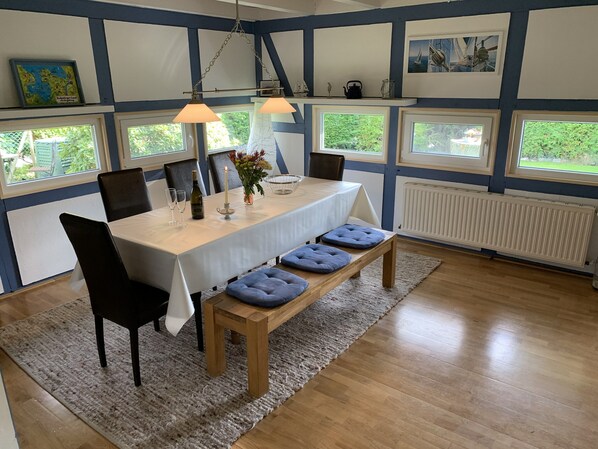 A dining area with a table, chairs, and benches. There are windows with views of greenery. - Spacious holiday home, close to the beach, WiFi, pets welcome, quiet residential area (Butjadingen - Burhave)