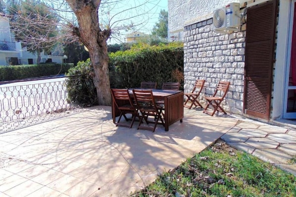 A patio with a table and chairs, a tree, and a stone wall.