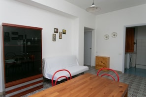 A room with a wooden table, a white sofa, a glass cabinet, and a wooden chest of drawers.