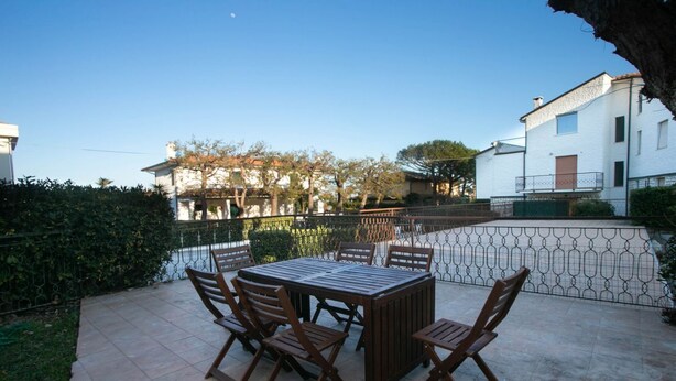 A patio with a table and chairs, a hedge, and a building in the background. - M084 - Marcelli, three-room apartment with garden at Residence MareVerde (Marcelli)