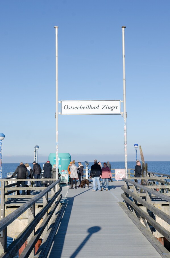 A pier with a sign reading "Ostseebad Zingst" and people walking along it.