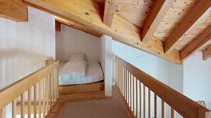 Una escalera estrecha conduce a un dormitorio con techo de madera y una cama blanca.