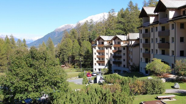 Un hotel de varios pisos con balcones, rodeado de abundante vegetación y montañas al fondo.