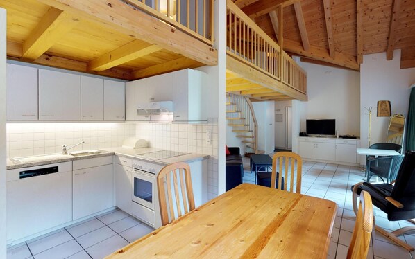 A modern kitchen with white cabinets, a wooden dining table, and a staircase leading to an upper level.